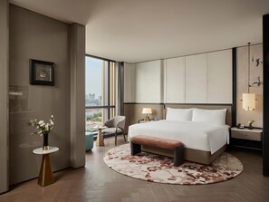 A modern hotel room with a large bed, a round rug, a small table with a vase of flowers, a chair, and a view of the city through large windows. - Intercontinental Changchun High Tech Zone (Changchun)