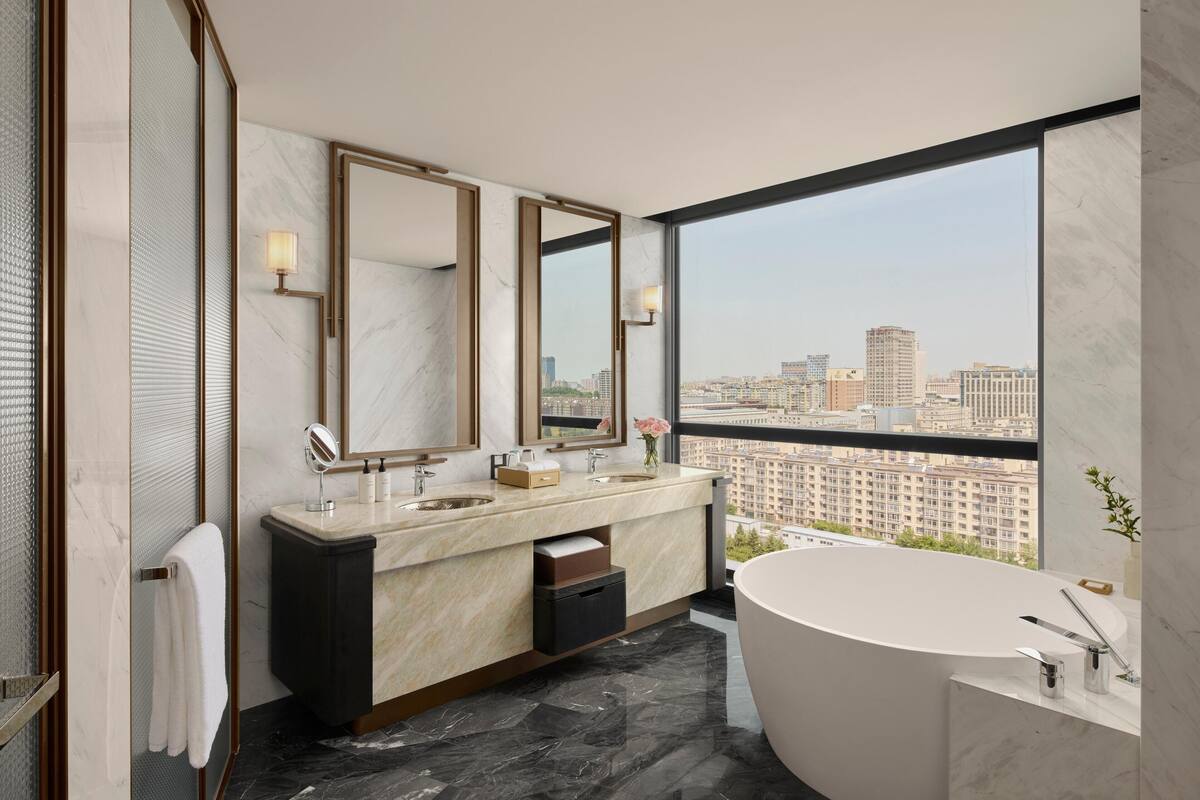 Een moderne badkamer met een ruime badkuip, twee wasbakken en een grote spiegel.