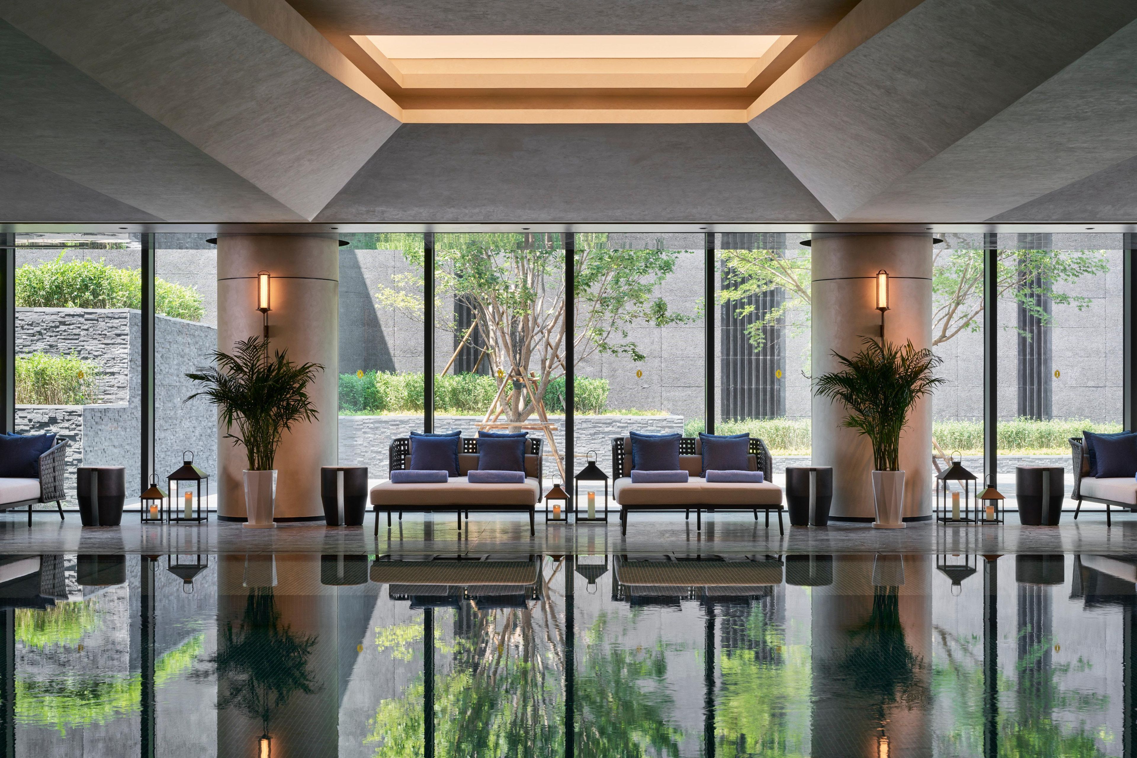 A modern lobby with a reflective floor, large windows, and a seating area with sofas and potted plants.