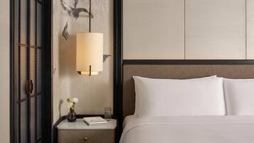 Een net opgemaakt bed met witte lakens, een nachtkastje met een lamp, een vaas met bloemen en een muur met een decoratieve vogelmuurschildering.