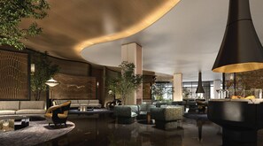 Een moderne lobby met een gebogen plafond, zithoeken en een grote, zwarte hanglamp.