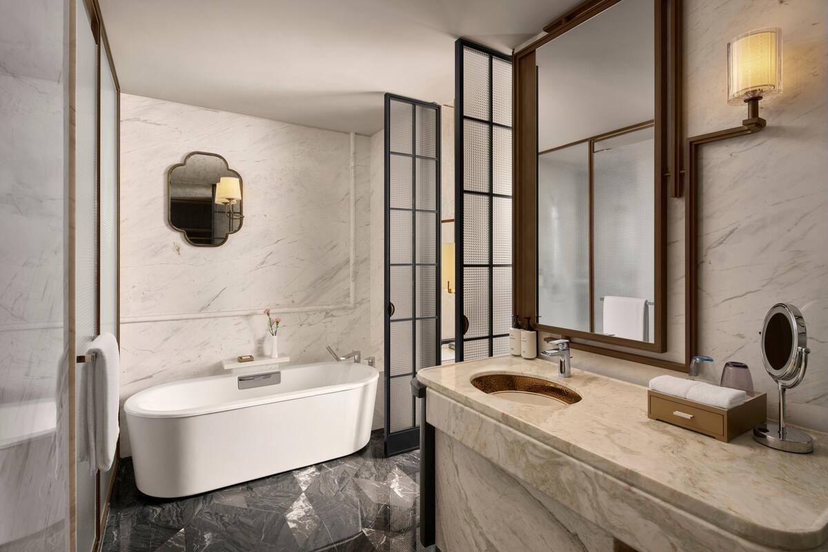 Een moderne badkamer met een vrijstaand bad, een grote spiegel en een marmeren aanrecht.