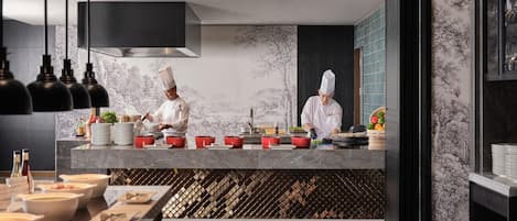A modern kitchen with chefs preparing food, marble countertops, and a wine rack.