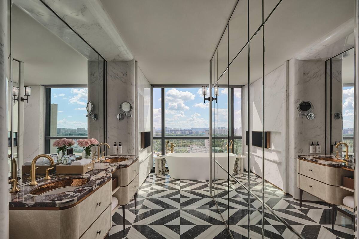 Een moderne badkamer met een groot bad, twee wastafels en een grote spiegel. De vloer heeft een zwart-wit geometrisch patroon.