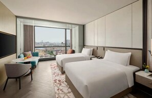 Ett hotellrum med två sängar, ett litet bord, en stol och ett stort fönster med utsikt över staden.