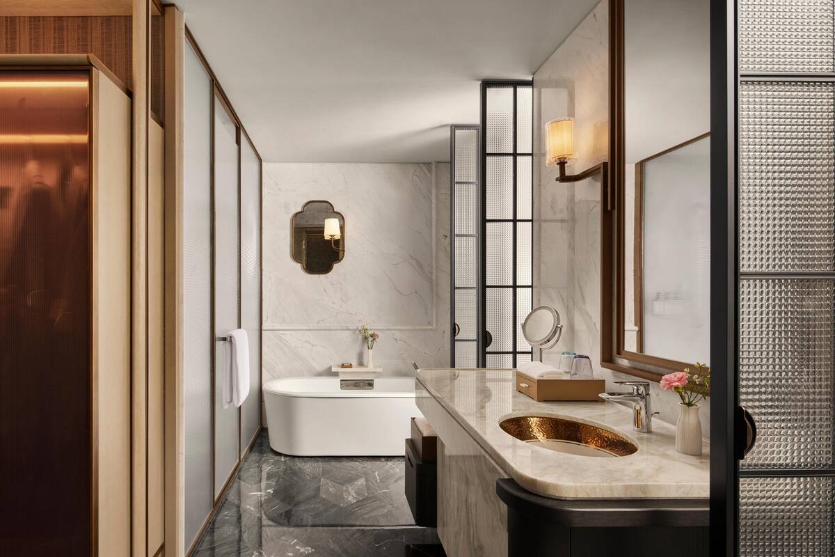 Een moderne badkamer met een vrijstaand bad, een wastafel met een gouden wasbak en een grote spiegel.
