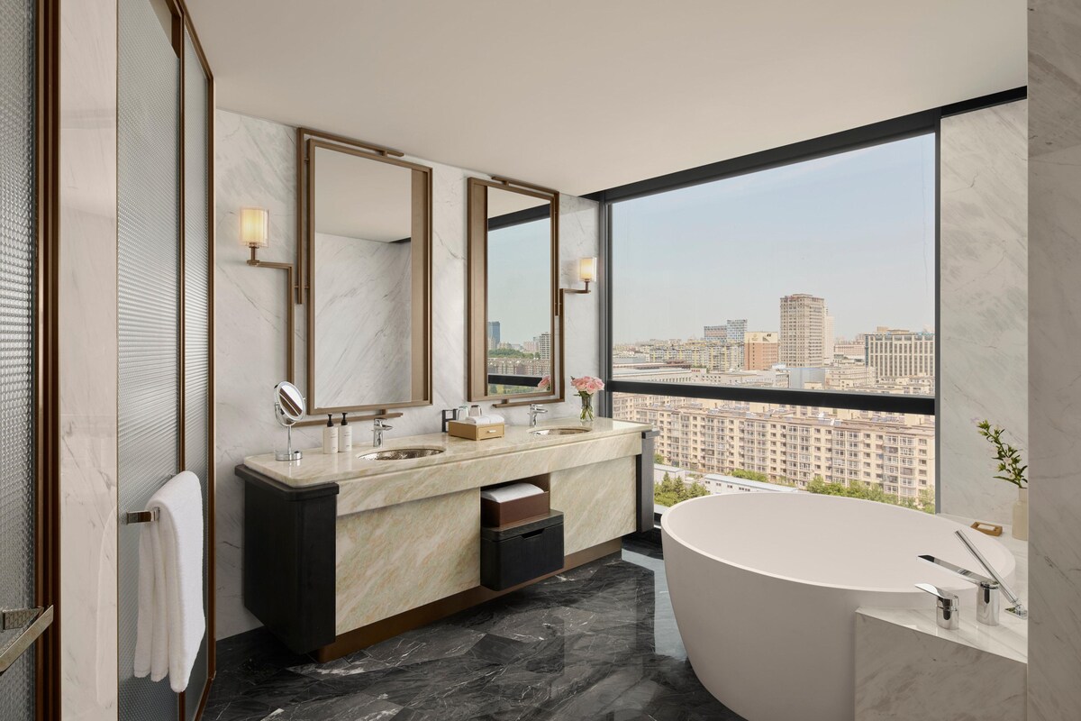 A modern bathroom with a large bathtub, two sinks, and a large mirror.