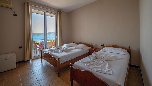 A room with two wooden beds, a sliding glass door leading to a balcony, and a radiator on the wall. - Hotel Nika Radhime (Vlorë)