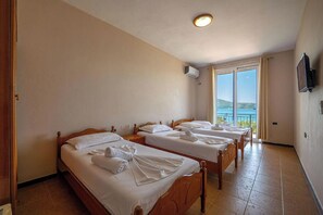A hotel room with three wooden beds, a TV mounted on the wall, and a large window offering a view of the sea. - Hotel Nika Radhime (Vlorë)