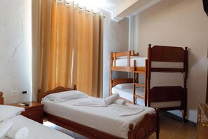 Ein Zimmer mit einem Einzelbett, einem hölzernen Etagenbett, einem Nachttisch mit Lampe und einem Fenster mit Vorhängen.