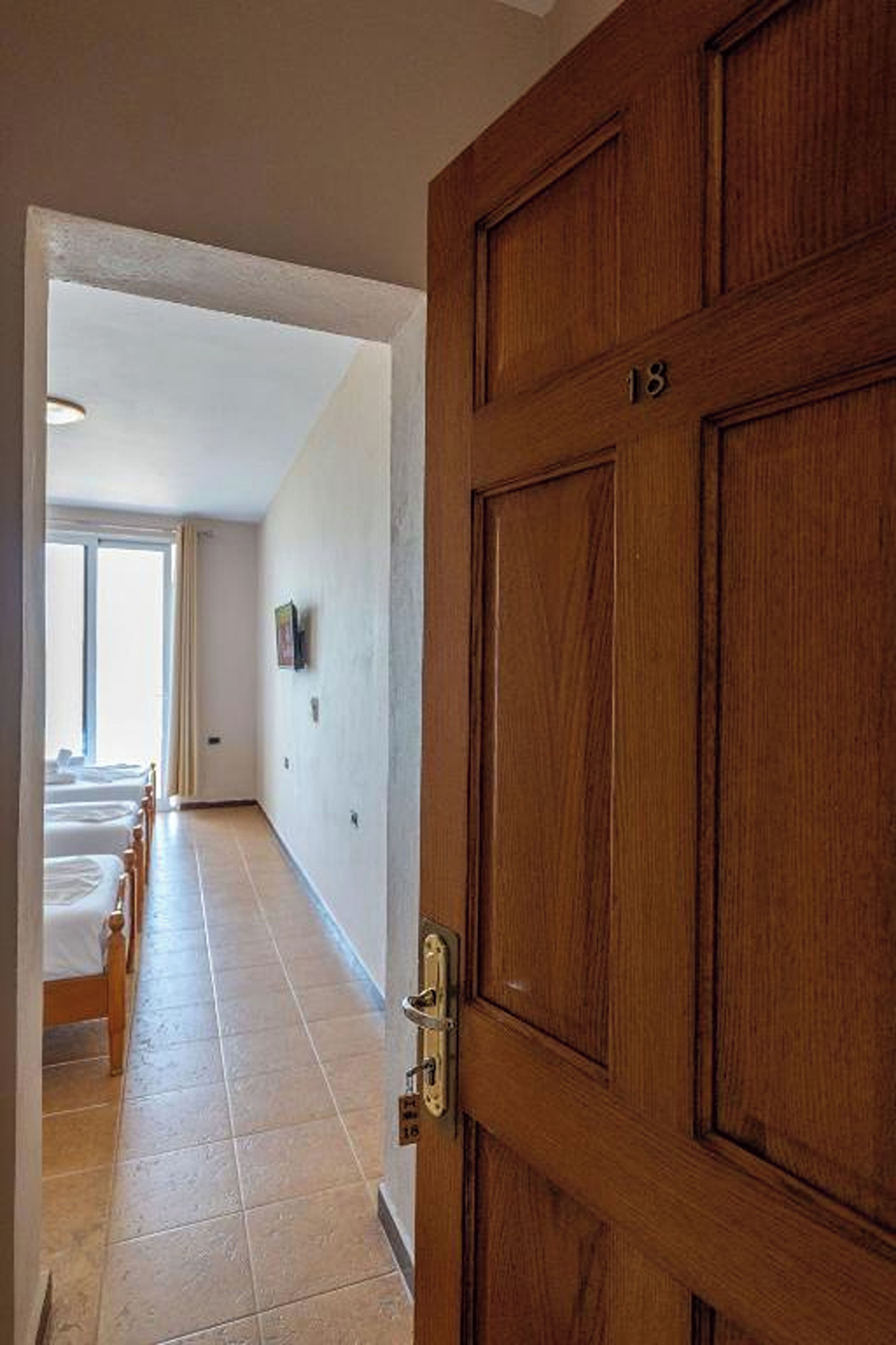 A hallway with a wooden door marked "18" leading to a room with a bed and a window.
