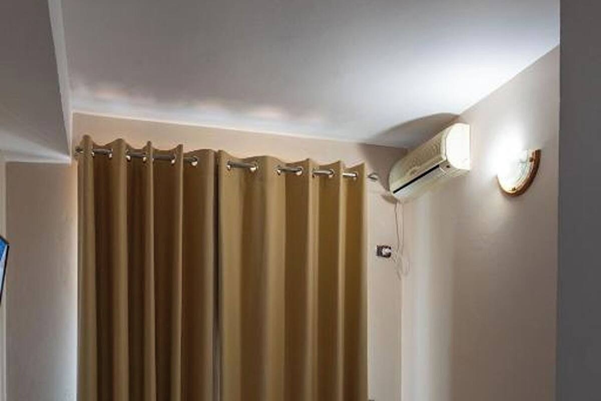 A hotel room with two beds, a bathroom with a shower curtain, and an air conditioning unit on the wall.