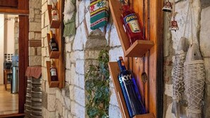 A stone wall with wooden shelves holding various bottles and a hanging plant. - Hotel Nika Radhime (Vlorë)