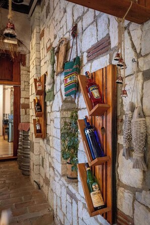 A stone wall with wooden shelves holding various bottles and a hanging plant. - Hotel Nika Radhime (Vlorë)