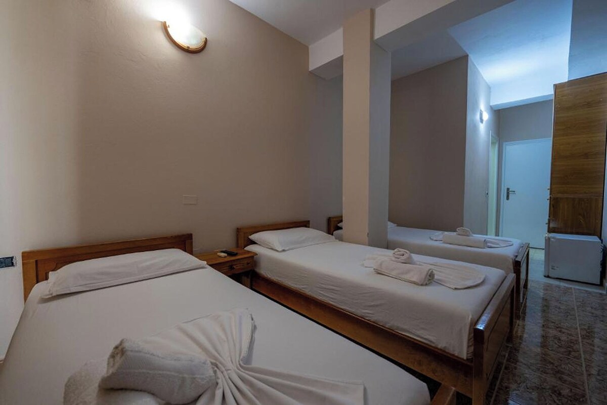 A hotel room with two single beds, a wooden headboard, a nightstand, a small table, and a wall-mounted light fixture.