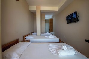 A hotel room with two beds, a flat-screen TV mounted on the wall, and a wooden headboard. - Hotel Nika Radhime (Vlorë)