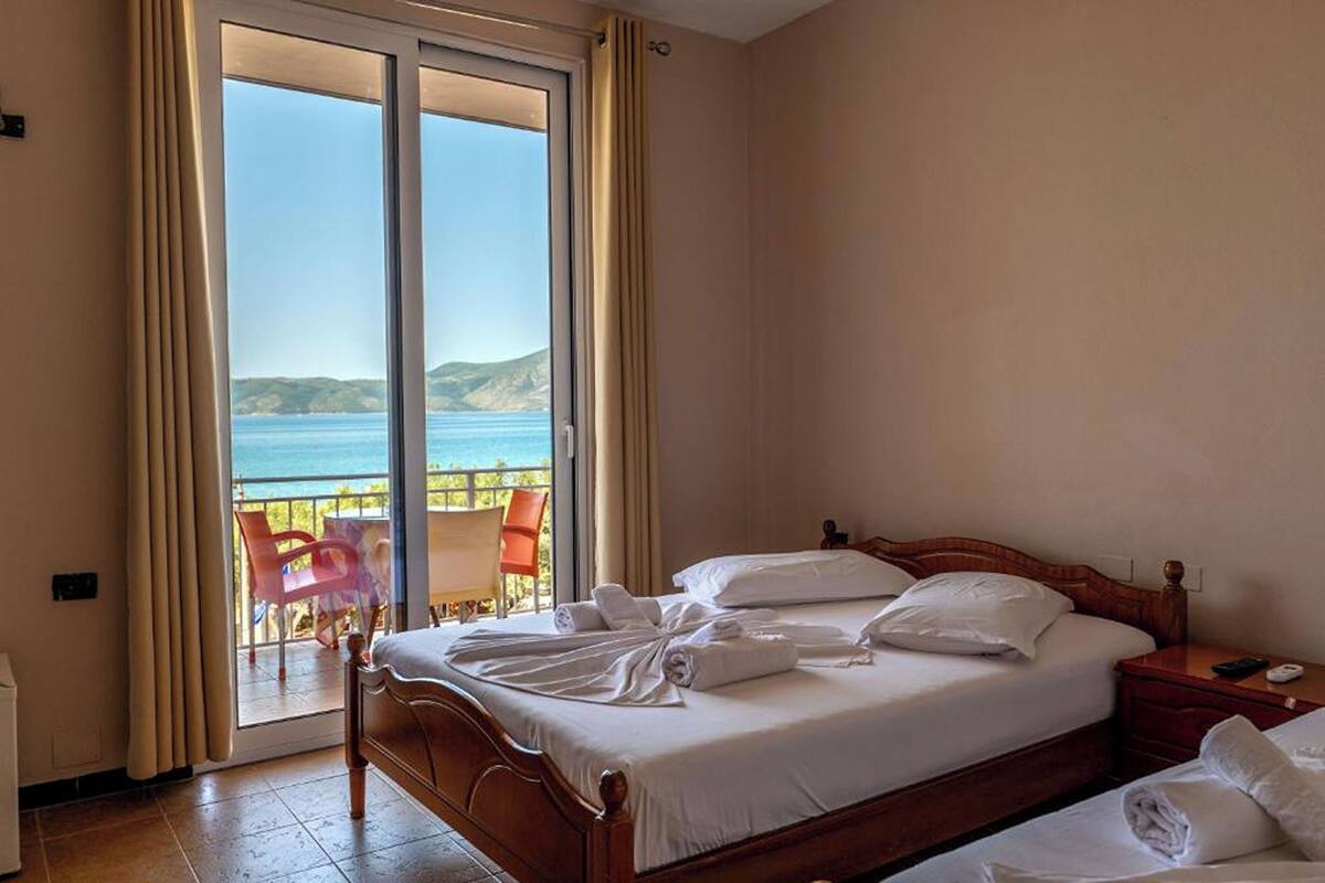 A hotel room with a bed, a nightstand, and a view of the sea through a sliding door.