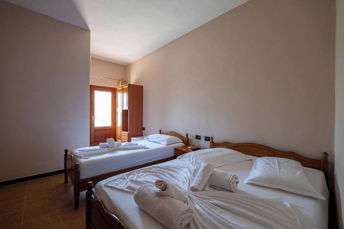 A hotel room with two beds, wooden headboards, white linens, and a wooden wardrobe.