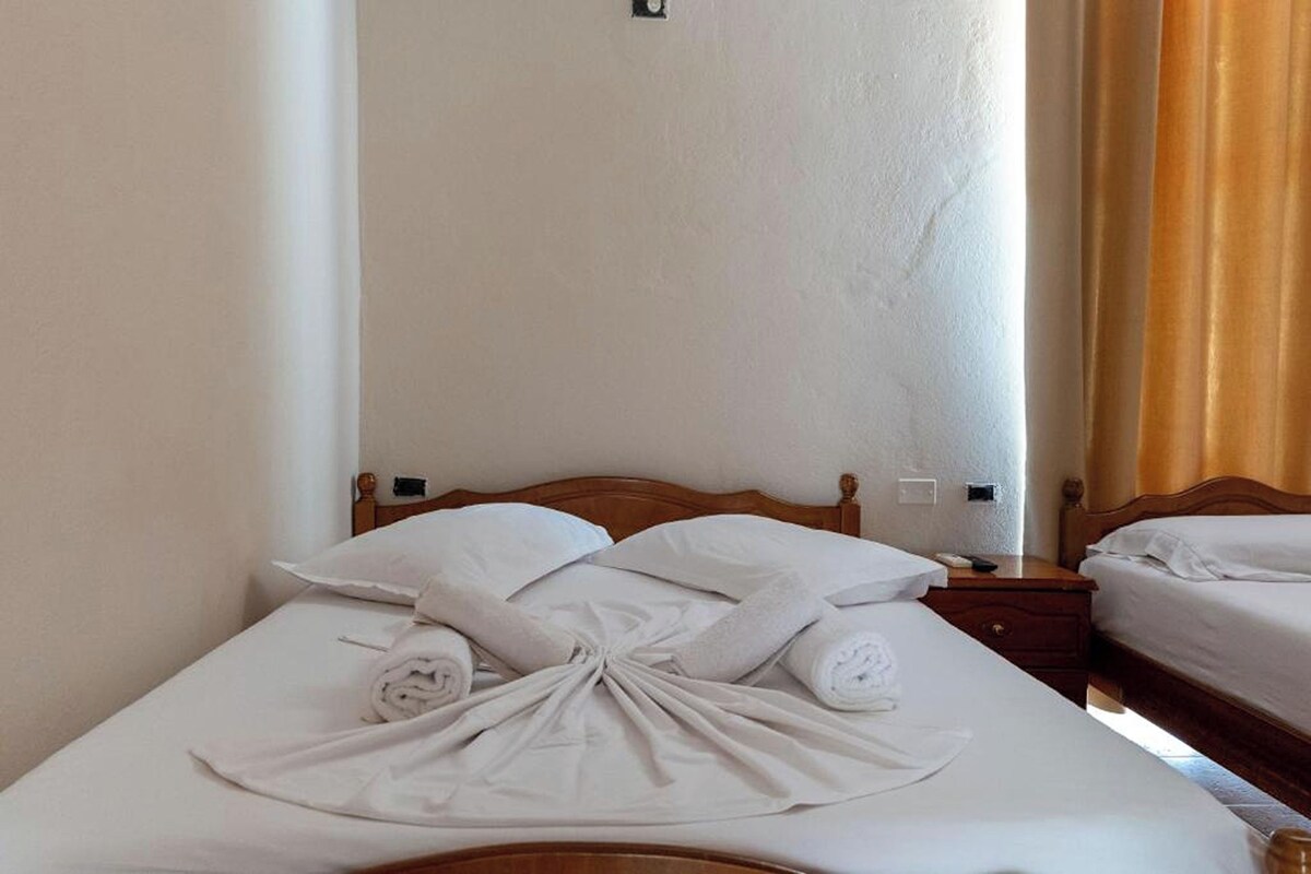 A hotel room with a neatly made bed, a wooden headboard, a bedside table, and a nightstand.