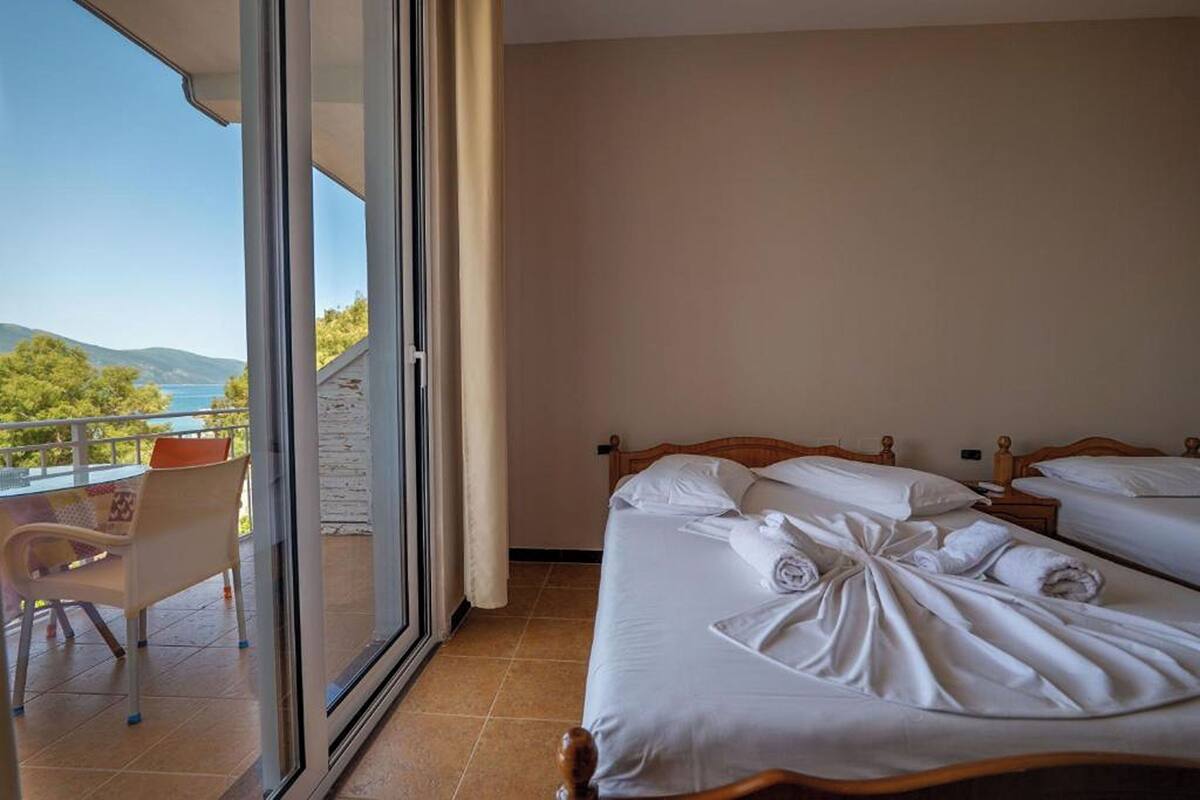 A hotel room with two beds, a balcony with a table and chairs, and a view of the sea and hills.