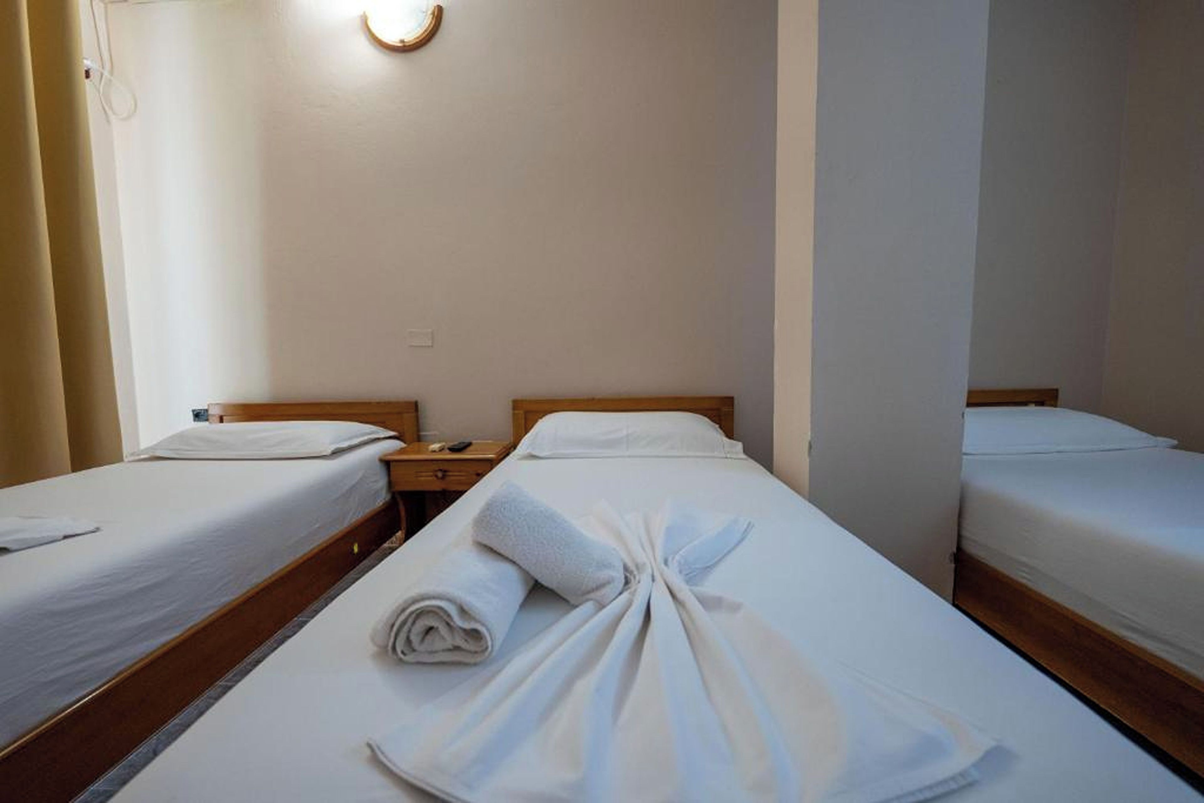 A hotel room with two single beds, each with a wooden headboard and white bedding. There is a nightstand with a lamp between the beds.