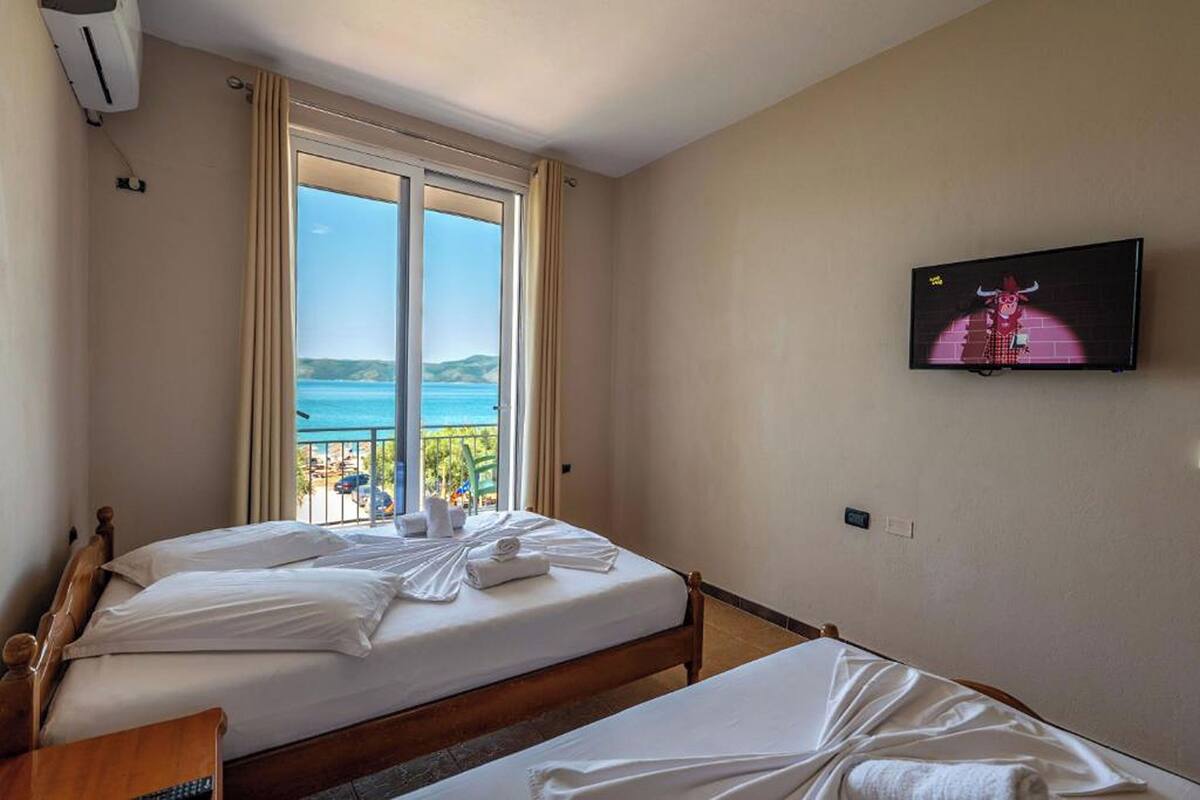 A hotel room with two beds, a television, and a balcony with a view of the sea.