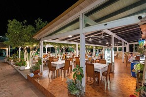 An outdoor dining area with tables and chairs, surrounded by potted plants and trees. - Hotel Nika Radhime (Vlorë)
