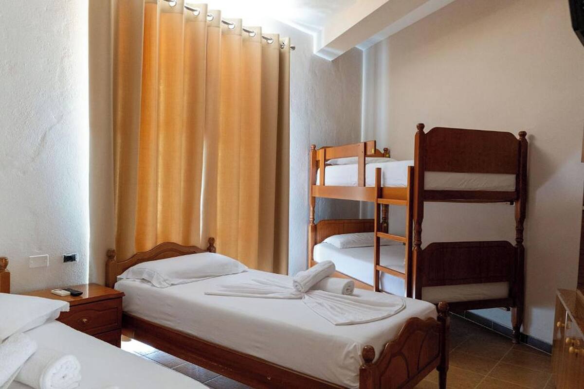 A room with a single bed, a wooden bunk bed, a nightstand with a lamp, and a window with curtains.