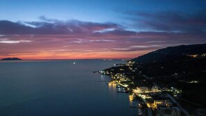 A coastal town at dusk with a calm sea, illuminated buildings, and a hilly backdrop. - Hotel Nika Radhime (Vlorë)