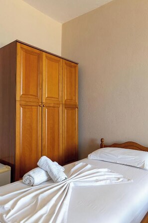 A hotel room with a wooden wardrobe, a neatly made bed with white linens, and a plain wall. - Hotel Nika Radhime (Vlorë)