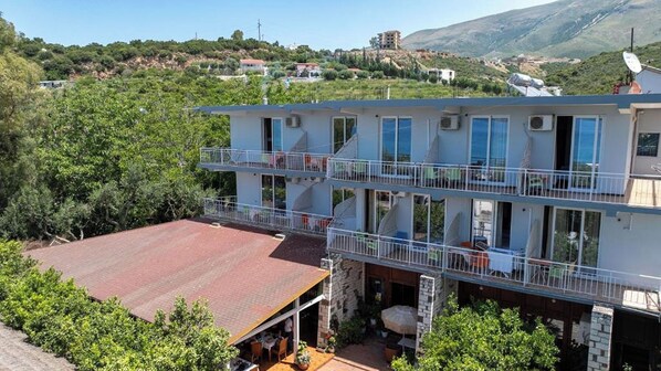 A multi-story building with balconies, a flat roof, and a view of a hillside. - Hotel Nika Radhime (Vlorë)