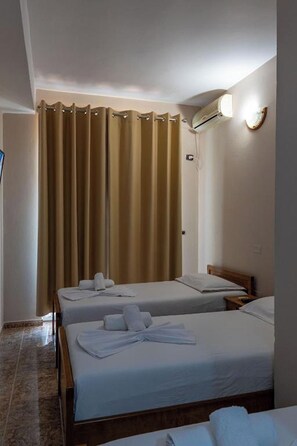 A hotel room with two beds, a bathroom with a shower curtain, and an air conditioning unit on the wall. - Hotel Nika Radhime (Vlorë)
