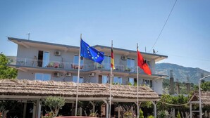 A two-story building with balconies, flags, and a thatched roof structure. - Hotel Nika Radhime (Vlorë)