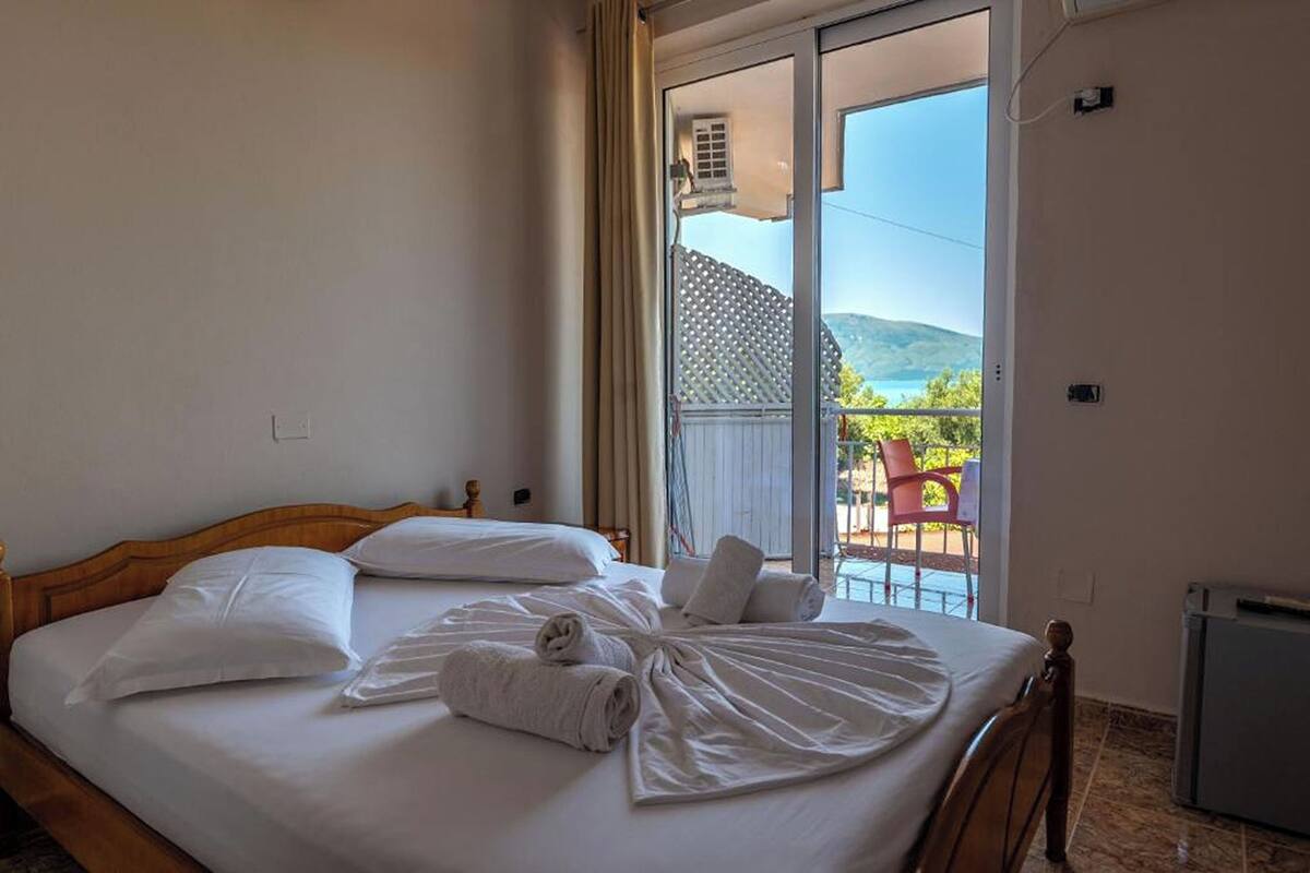 A hotel room with a bed, a view of the outdoors, and a balcony with chairs.