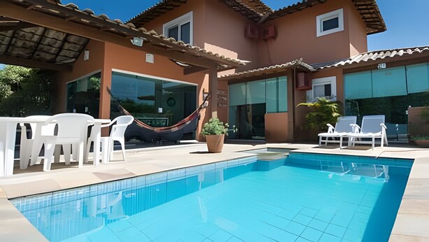 Piscina com cadeiras de descanso brancas e uma rede.
