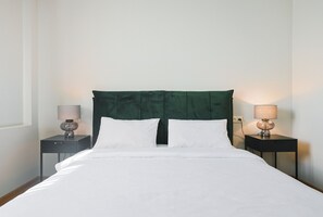 A neatly made bed with a green headboard, two bedside tables with lamps, and a plain white wall. - Hotel White House (Tbilisi)