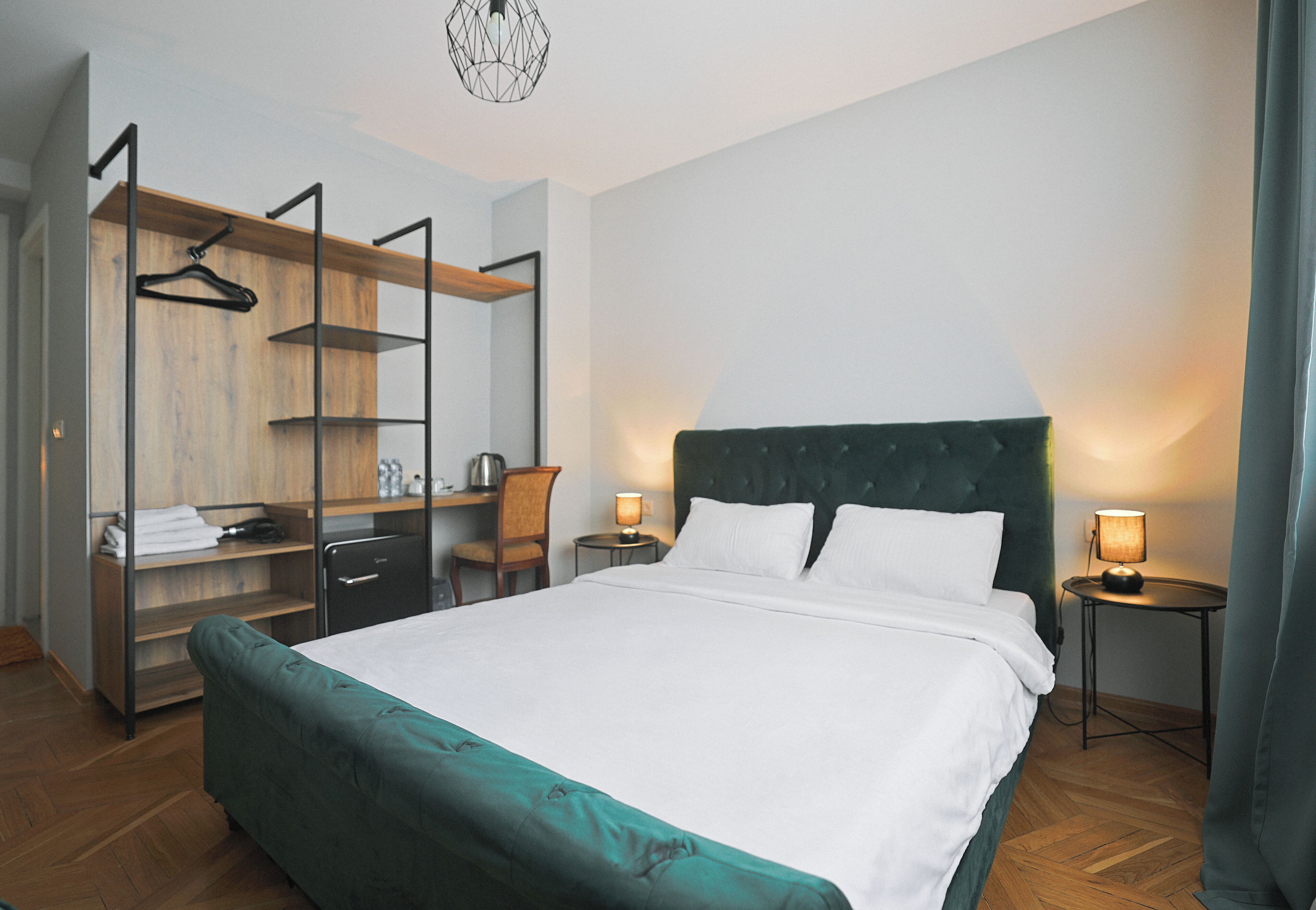 A hotel room with a large bed, a desk with a chair, a wardrobe, and two bedside tables with lamps.