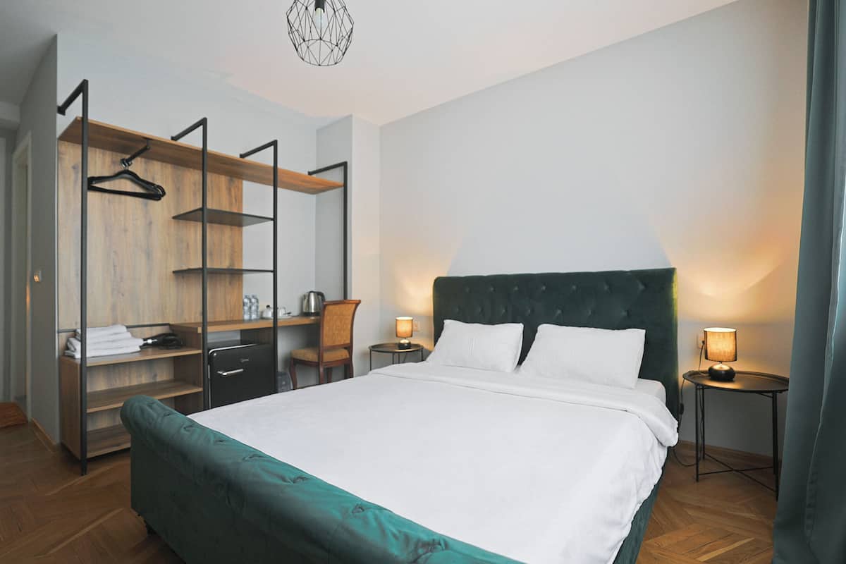 A hotel room with a large bed, a desk with a chair, a wardrobe, and two bedside tables with lamps.