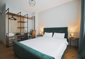 Habitación de hotel con una cama grande, un escritorio con silla, un armario y dos mesitas de noche con lámparas.