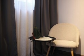 Une pièce avec une chaise, une petite table, une plante en pot et une fenêtre avec des rideaux.