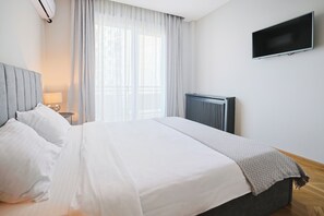 Una cama bien hecha con sábanas blancas, cabecera gris y una manta gris.