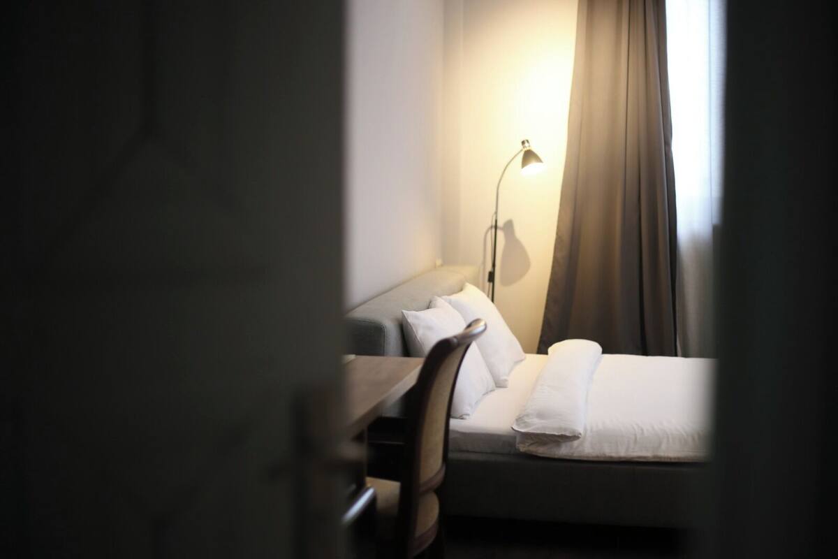 A hotel room with a bed, a desk, a chair, a lamp, and a window with curtains.