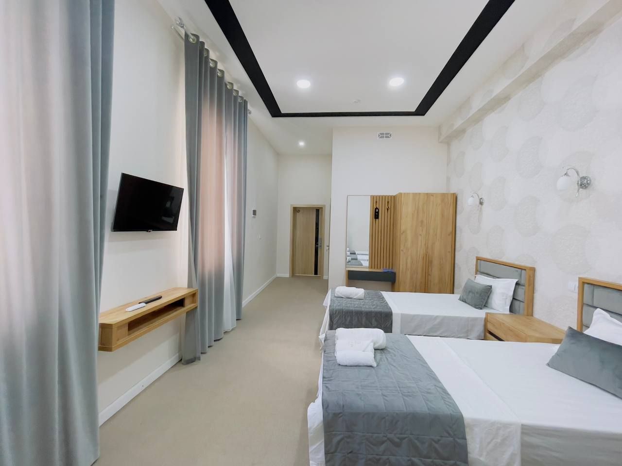 A hotel room with two beds, a TV, a wooden wardrobe, and a mirror.