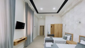 A hotel room with two beds, a TV, a wooden wardrobe, and a mirror. - Emin Hotel (Margilan)