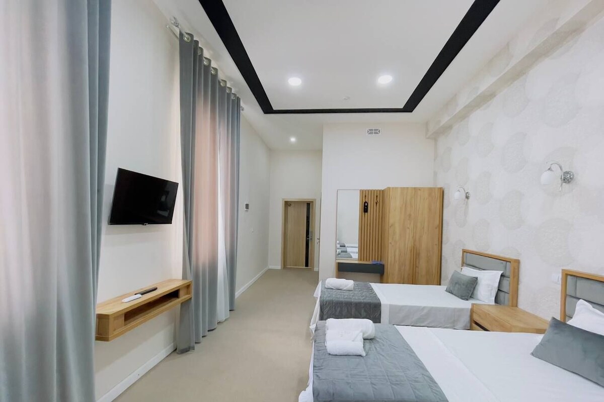 A hotel room with two beds, a TV, a wooden wardrobe, and a mirror.