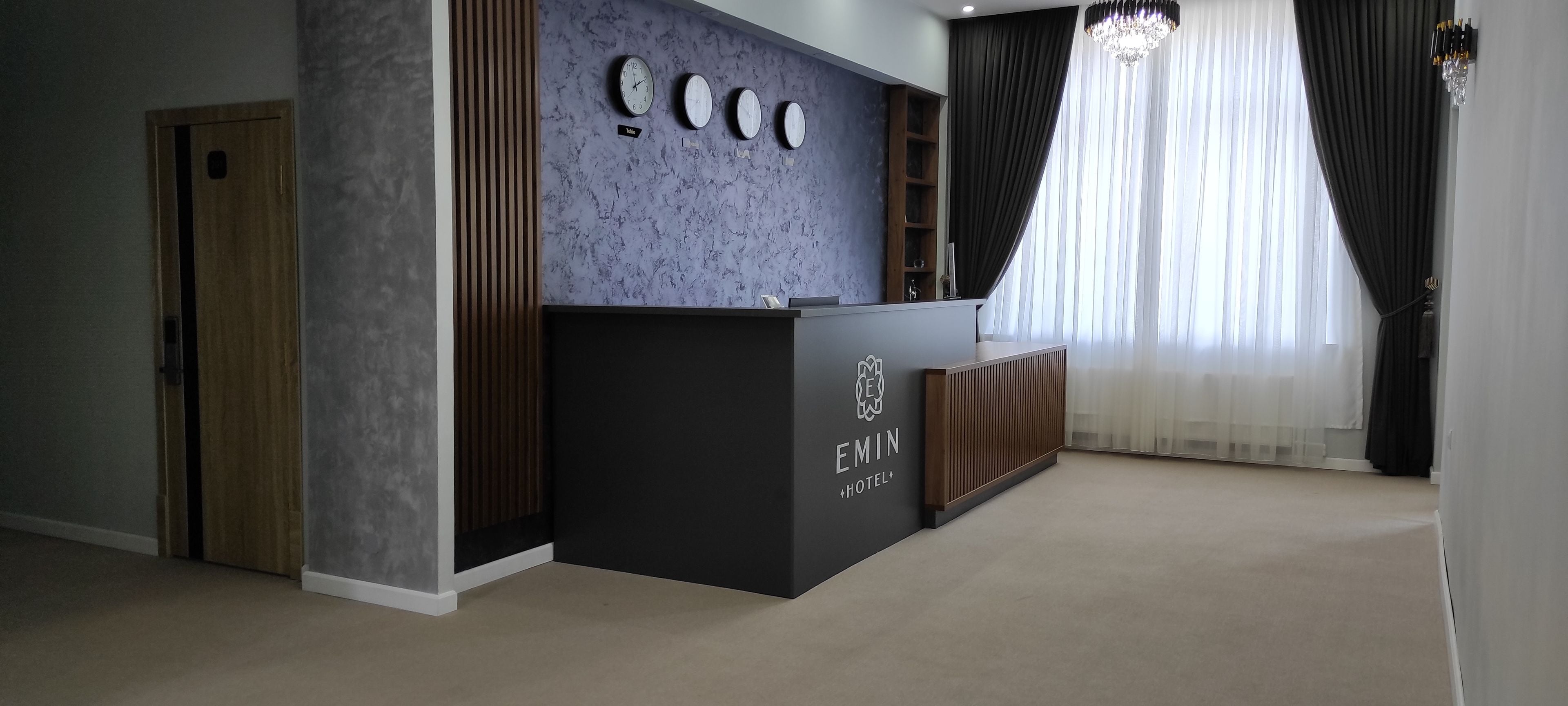 A hotel reception desk with a marble wall, clocks, and a sign that reads "EMIN HOTEL".