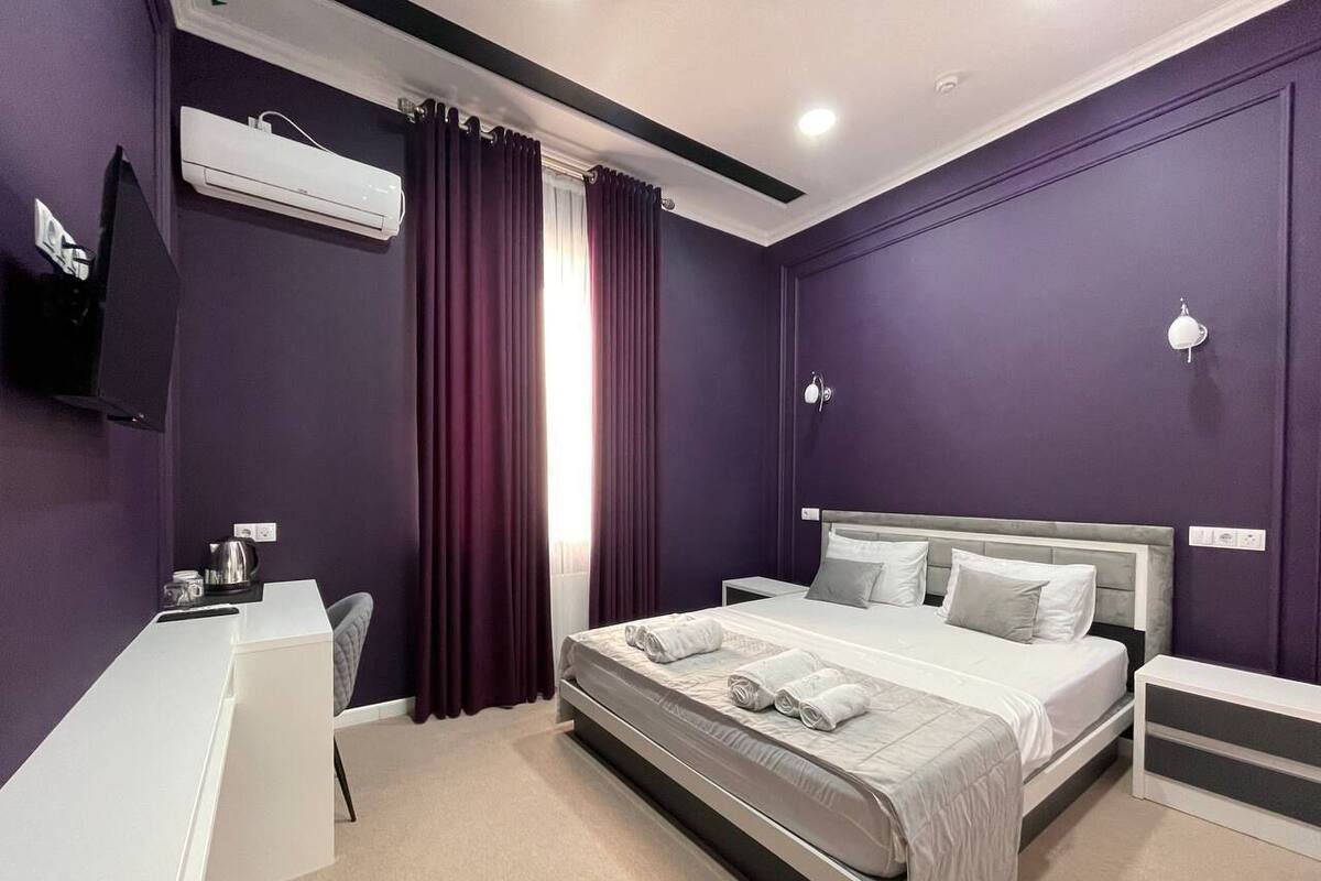 A modern hotel room with a bed, a desk, and an air conditioning unit.