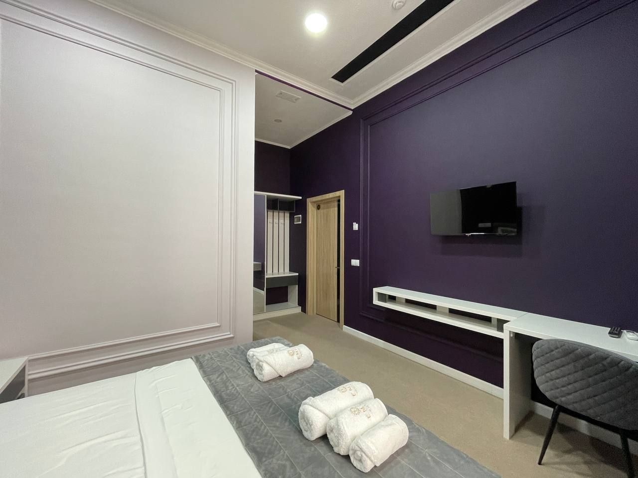A hotel room with a bed, a desk, a TV, and towels on the bed.