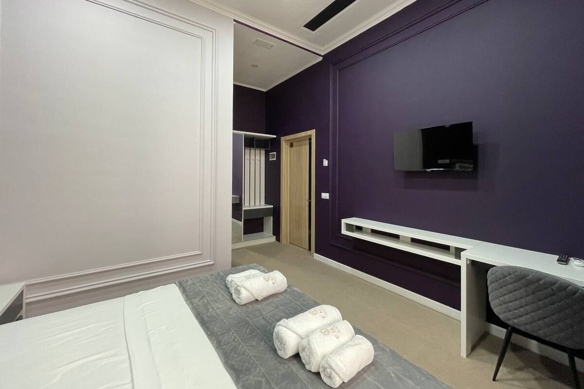A hotel room with a bed, a desk, a TV, and towels on the bed.