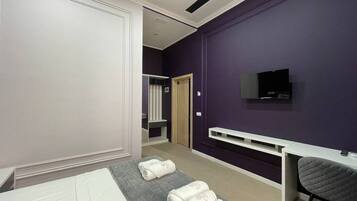 A hotel room with a bed, a desk, a TV, and towels on the bed.